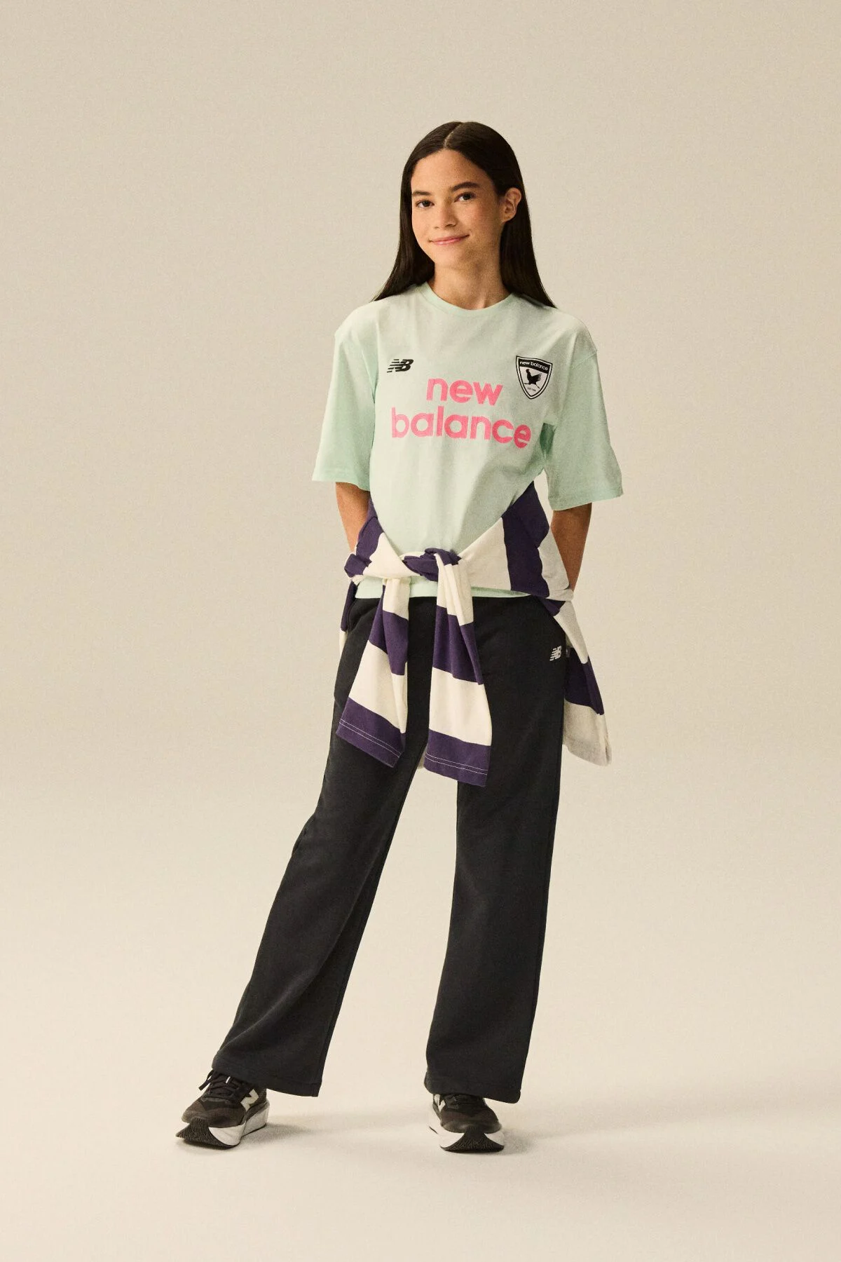 Young kid standing in front of a bike wearing blue jeans and a pink shirt. 