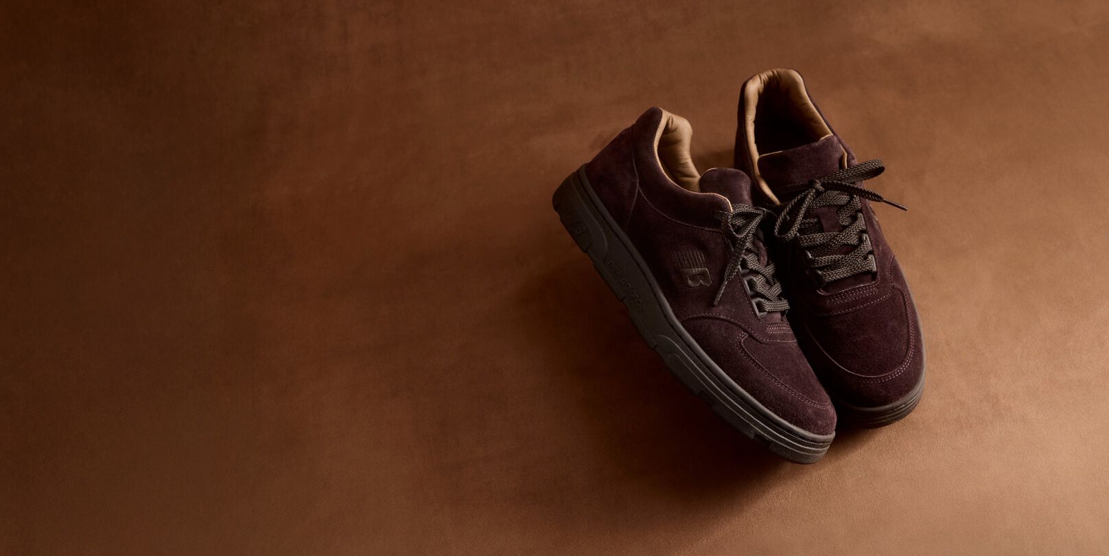 A pair of New Balance Made in UK sneakers in a brown textured studio environment. 