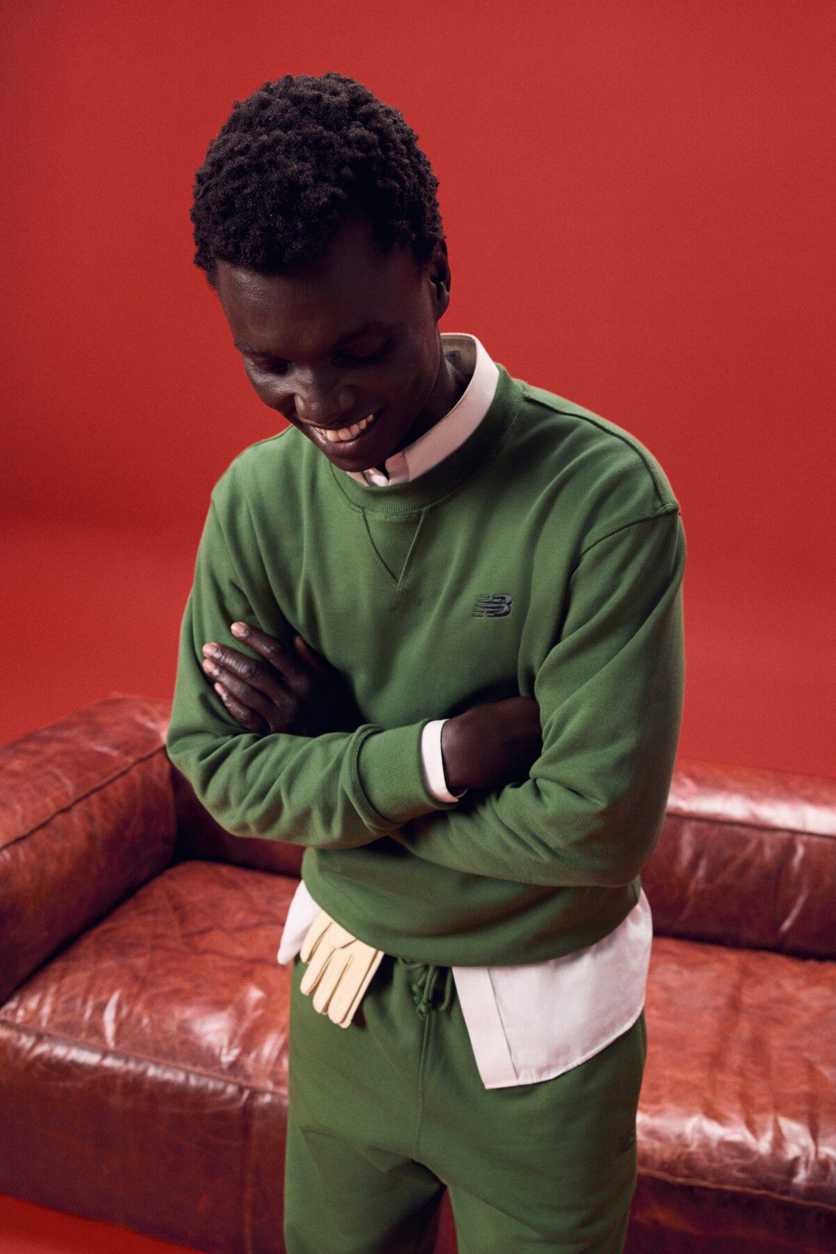 Man wearing a green outfit laughing in front of a red couch.