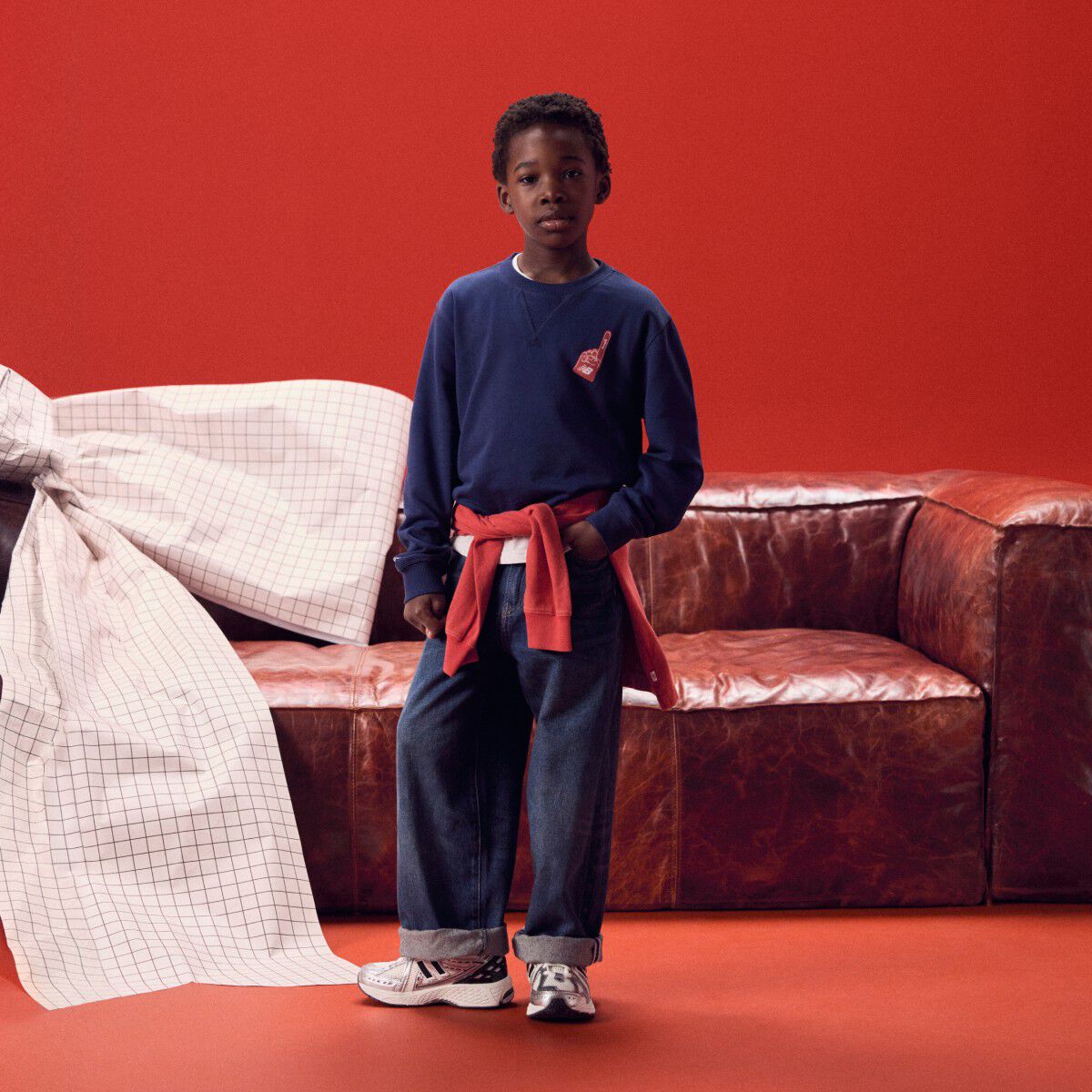 Kid wearing a navy long sleeve shirt in front of a red couch.
