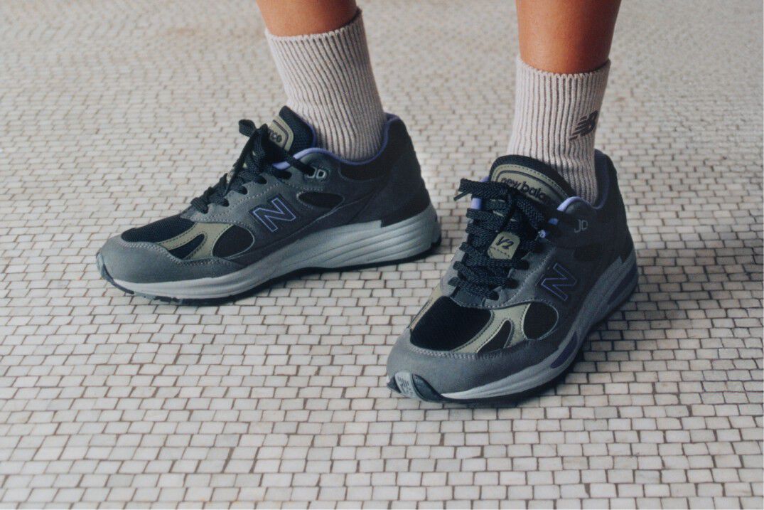 Feet view of a woman wearing a pair of New Balance Made in UK sneakers standing on a white tiled floor.